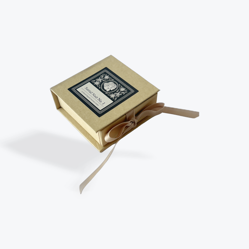 A square kraft paper gift box with a black decorative label on top and a beige ribbon tied in a bow, shown floating against a light gray background.