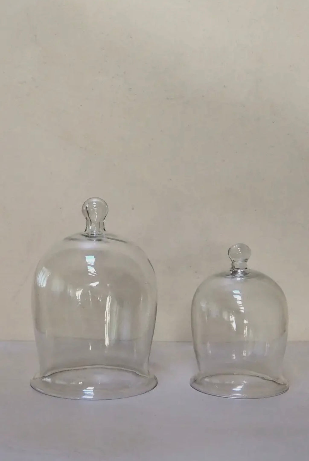 Two clear glass domes on a white surface with a beige background