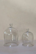 Two clear glass domes on a white surface with a beige background