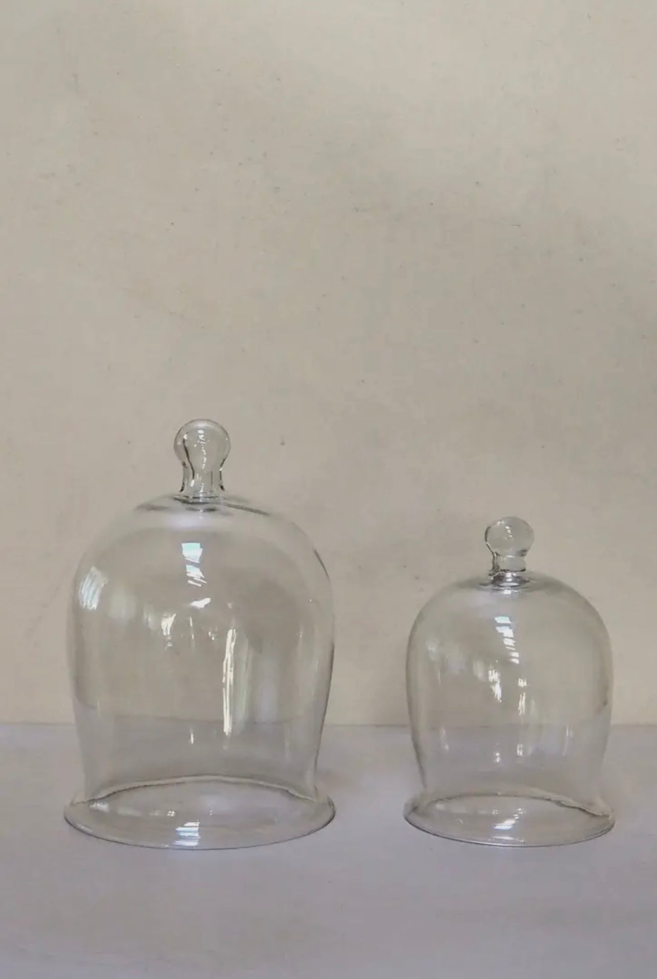 Two clear glass domes on a white surface with a beige background
