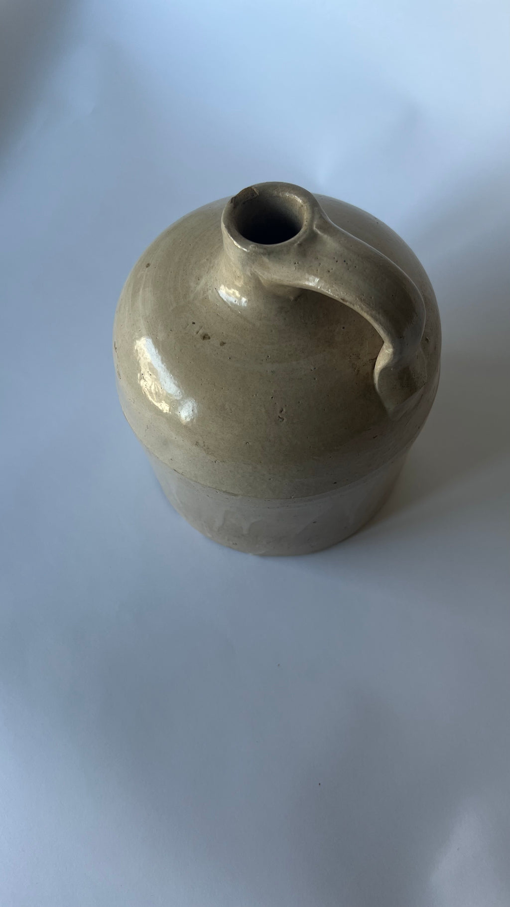 A small handmade ceramic jug with a rounded body, a side handle, and a short spout, glazed in a light beige-green glaze on a plain white background.