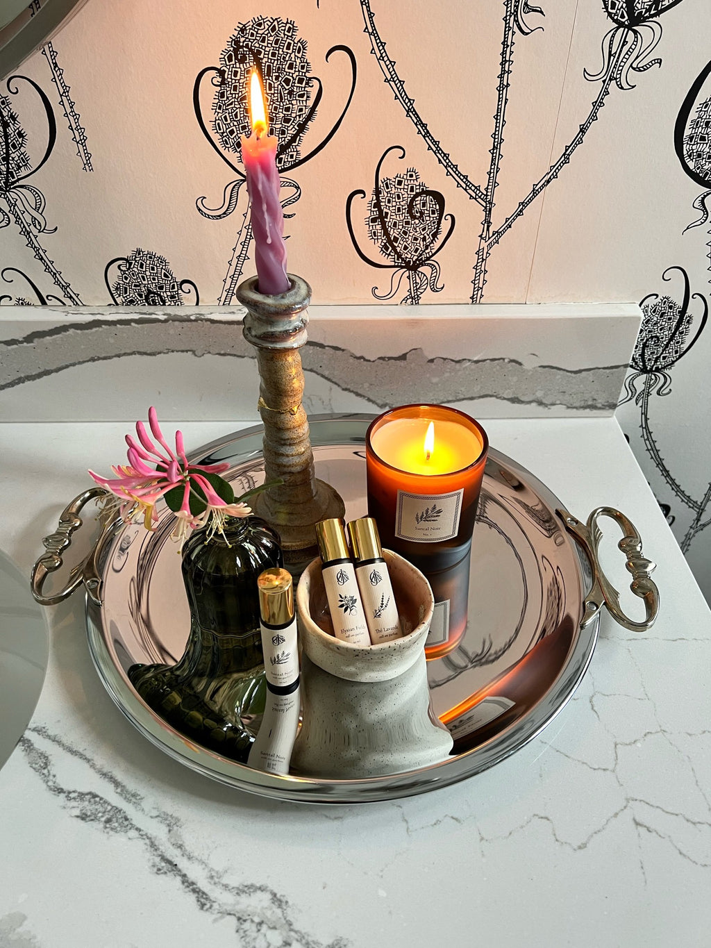 Kromex tray with candle, roll on parfum, and a small flower on a marble surface.