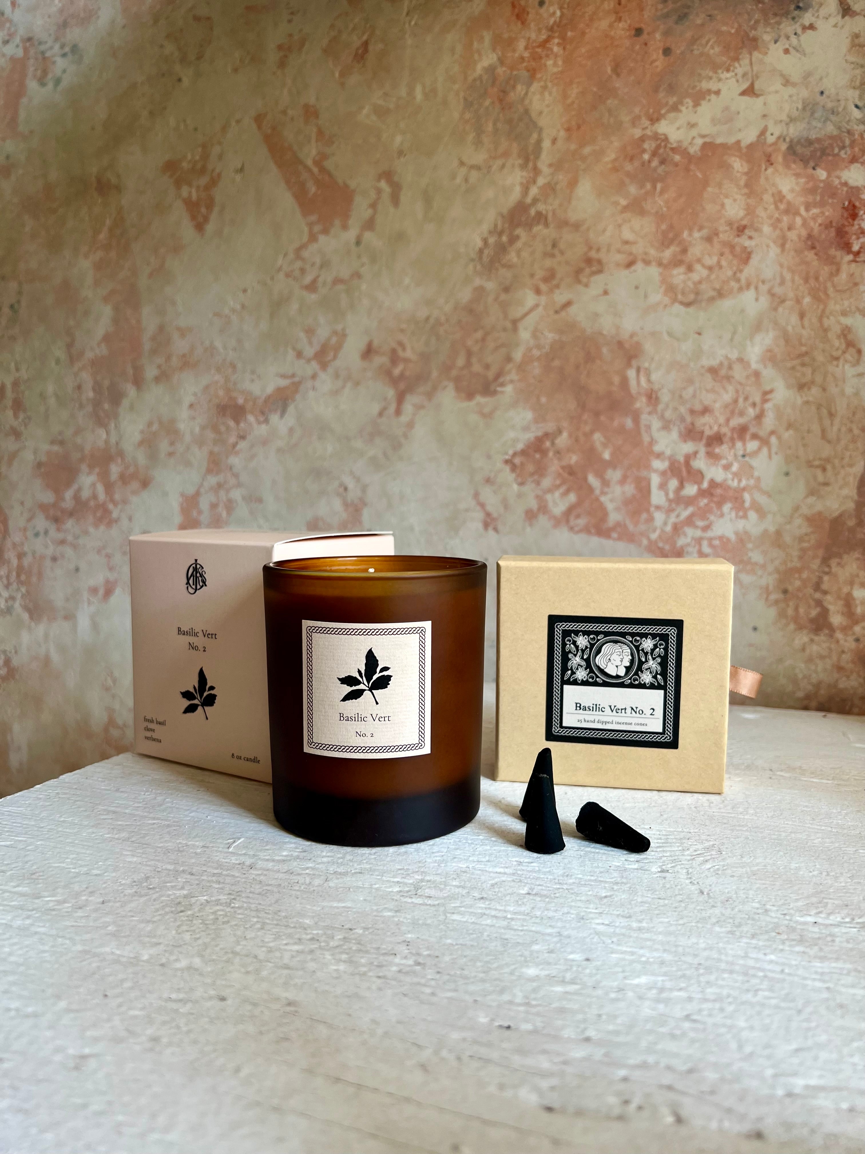 Candle with packaging and black incense cones on a textured surface