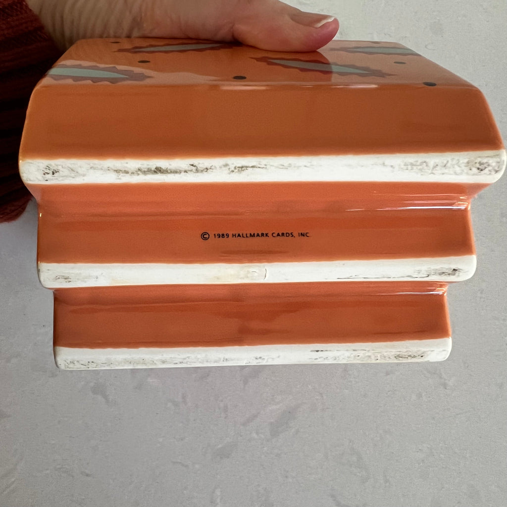 A hand holding the bottom of a small ceramic container with a light background