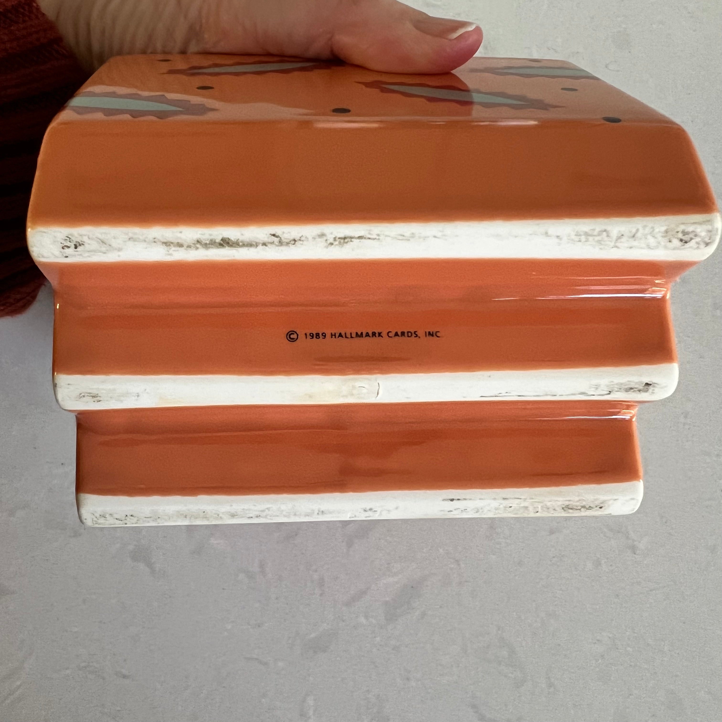 A hand holding the bottom of a small ceramic container with a light background