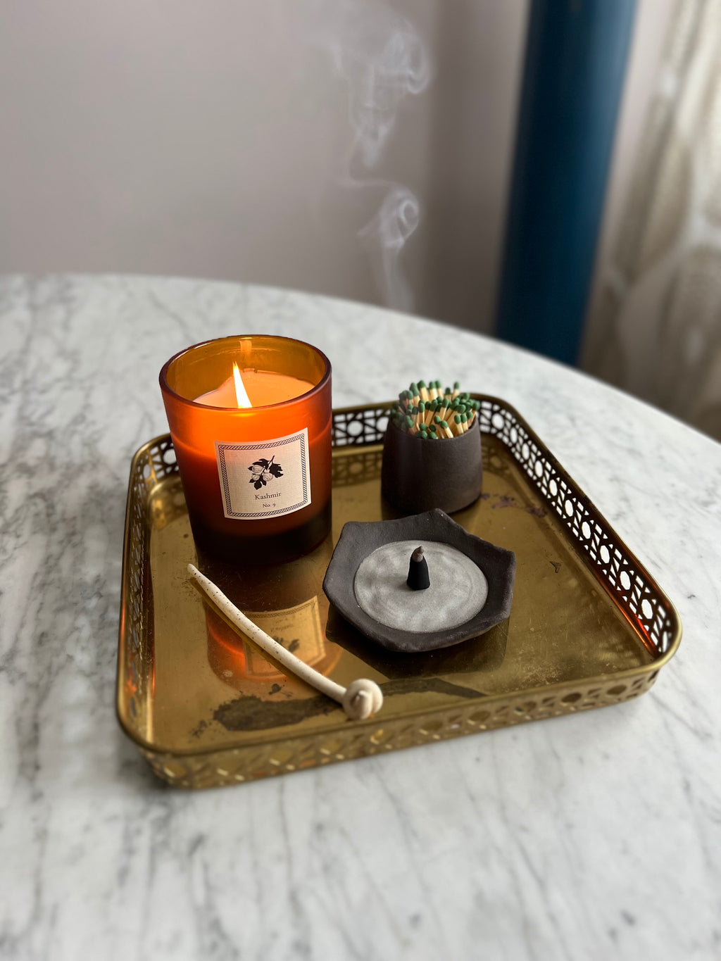 A candle, a match strike and small dish on a decorative tray on a marble surface.