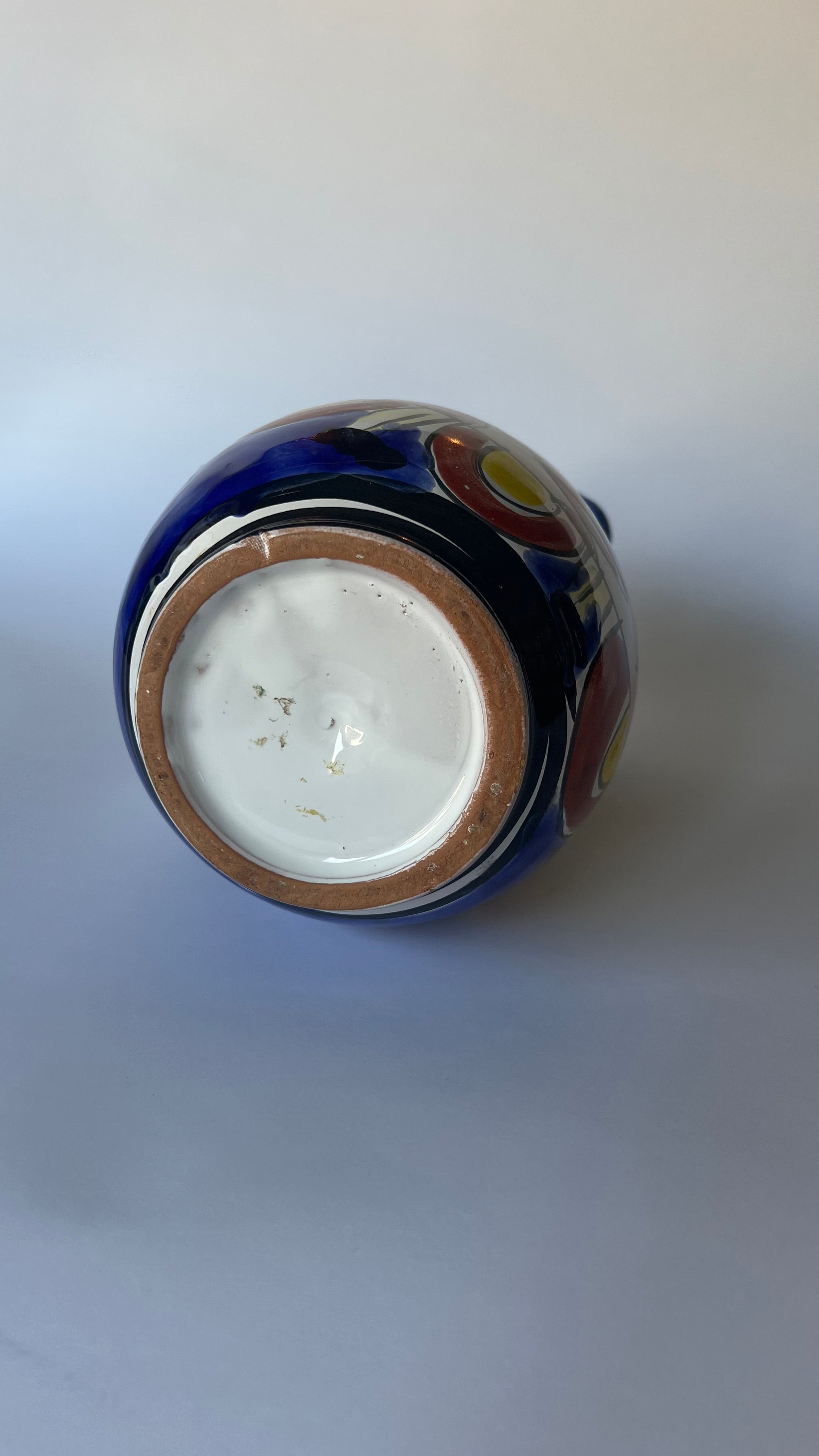 A close-up shot of the bottom of a ceramic pitcher, showing a glossy dark blue exterior with hand-painted multicolor motifs and a white glazed interior base.