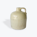 A vintage ceramic jugs with a rounded body, short neck, and side handle, glazed in a light cream-beige stoneware finish, shown on a plain white background.