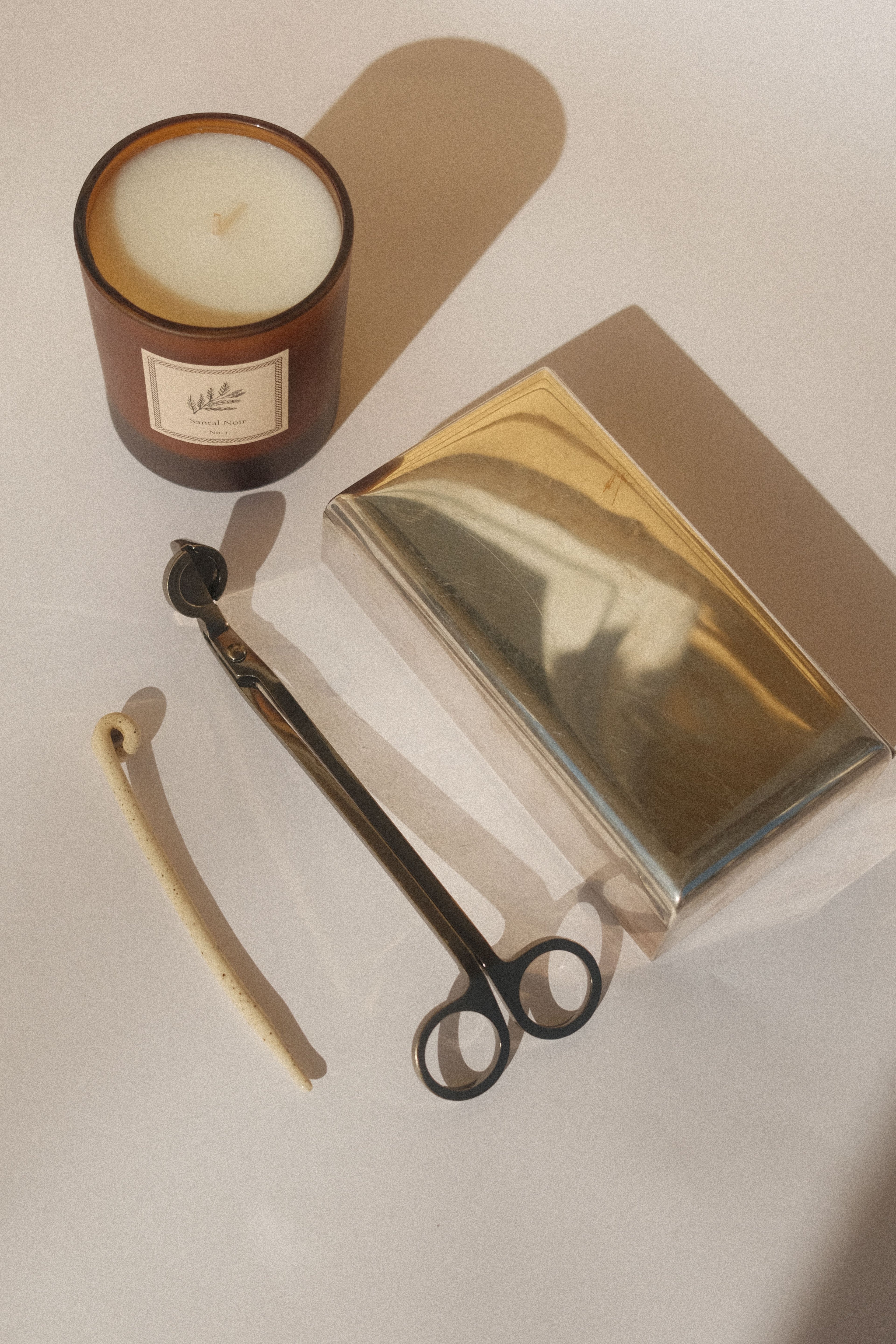 A white tabletop featuring a candle and candle accessories with sunlit shadows.