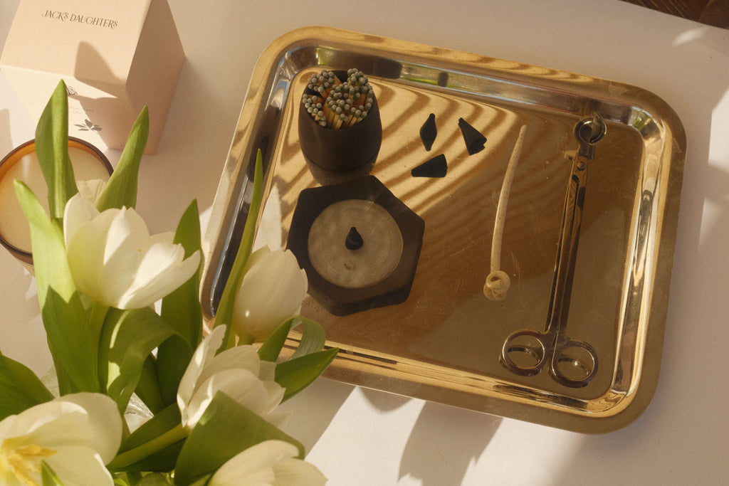 A tabletop featuring white tulips and incense, matches, and candle accessories a on a silver tray.
