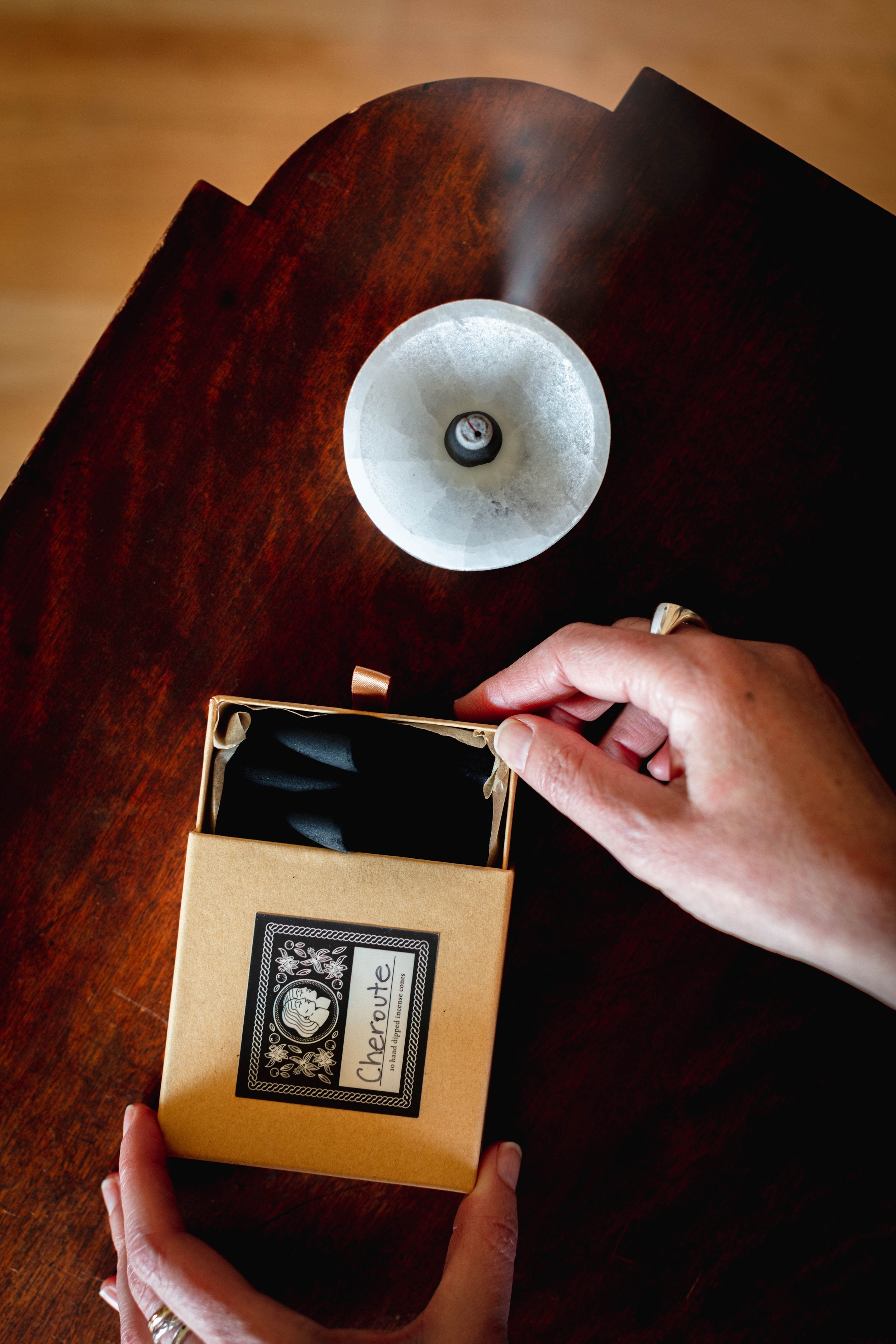 Person opening an incense box with a black interior on a wooden surface.