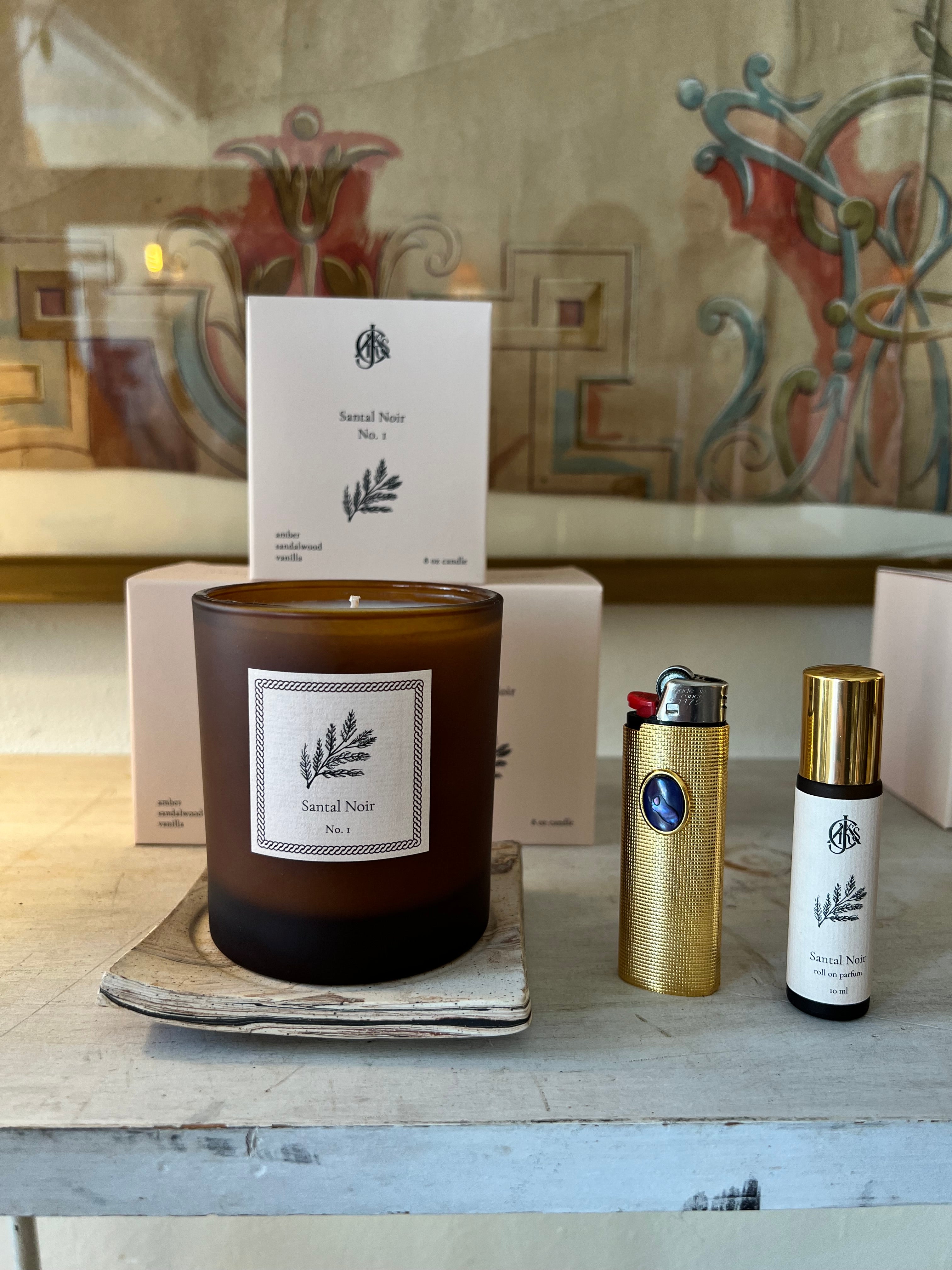 A candle, lighter case and roll on perfume on a wooden surface with a patterned background