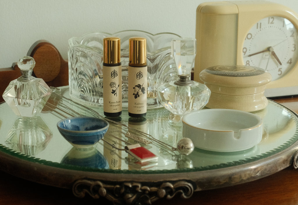 Tabletop scene with perfume bottles, jewelry, a clock, and decorative items on a mirrored tray.