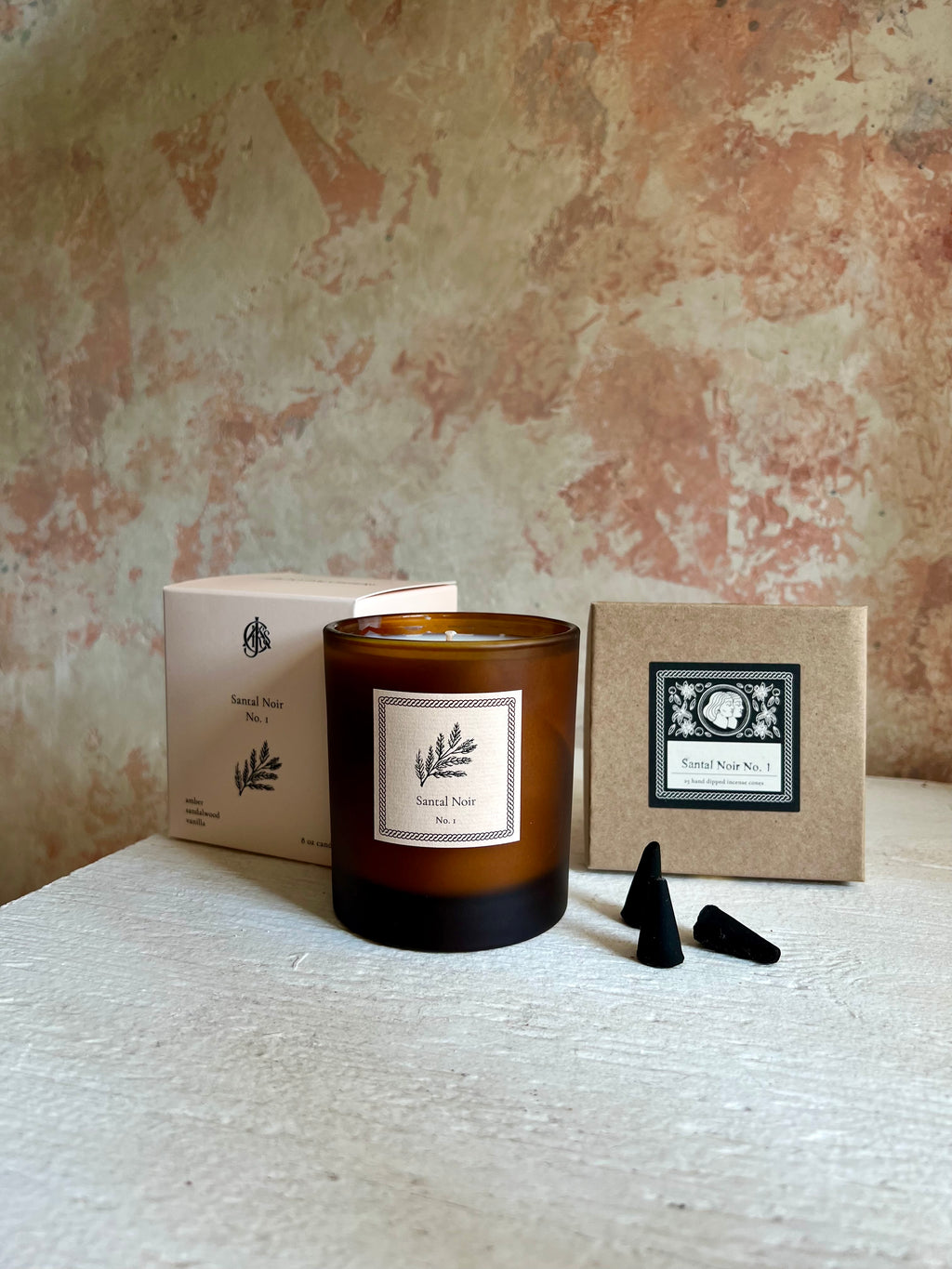 Candle with packaging and incense cones on a textured surface