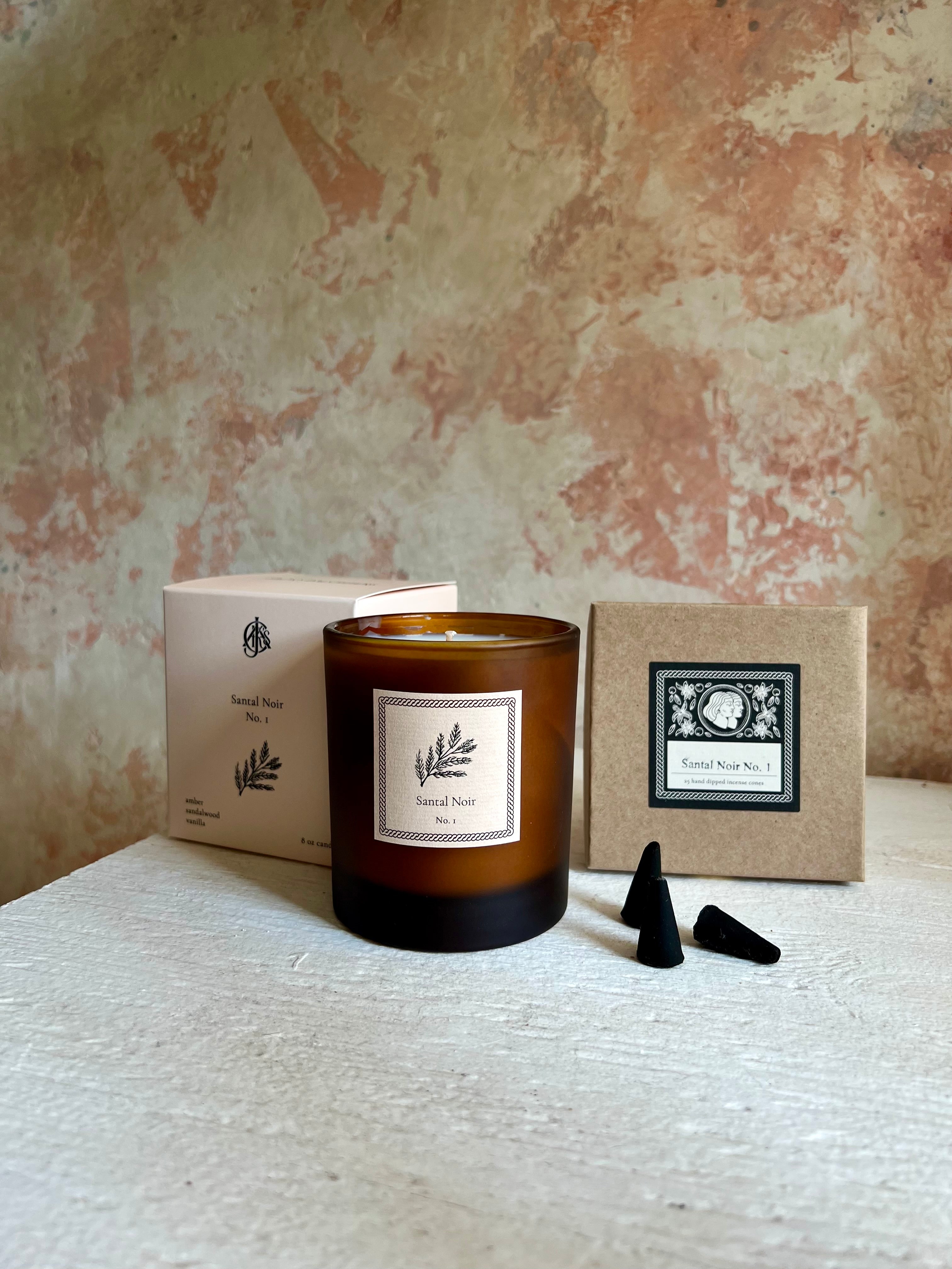 Candle with packaging and incense cones on a textured surface