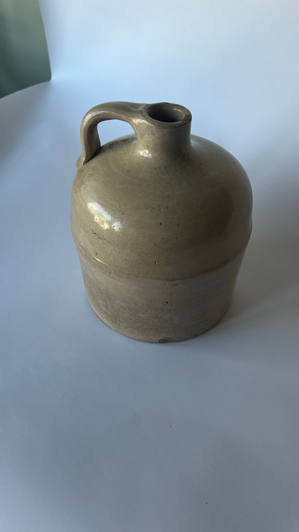 A vintage stoneware jug with a rounded body, a single loop handle, and a short neck, glazed in a matte, speckled light brown or beige ceramic finish.