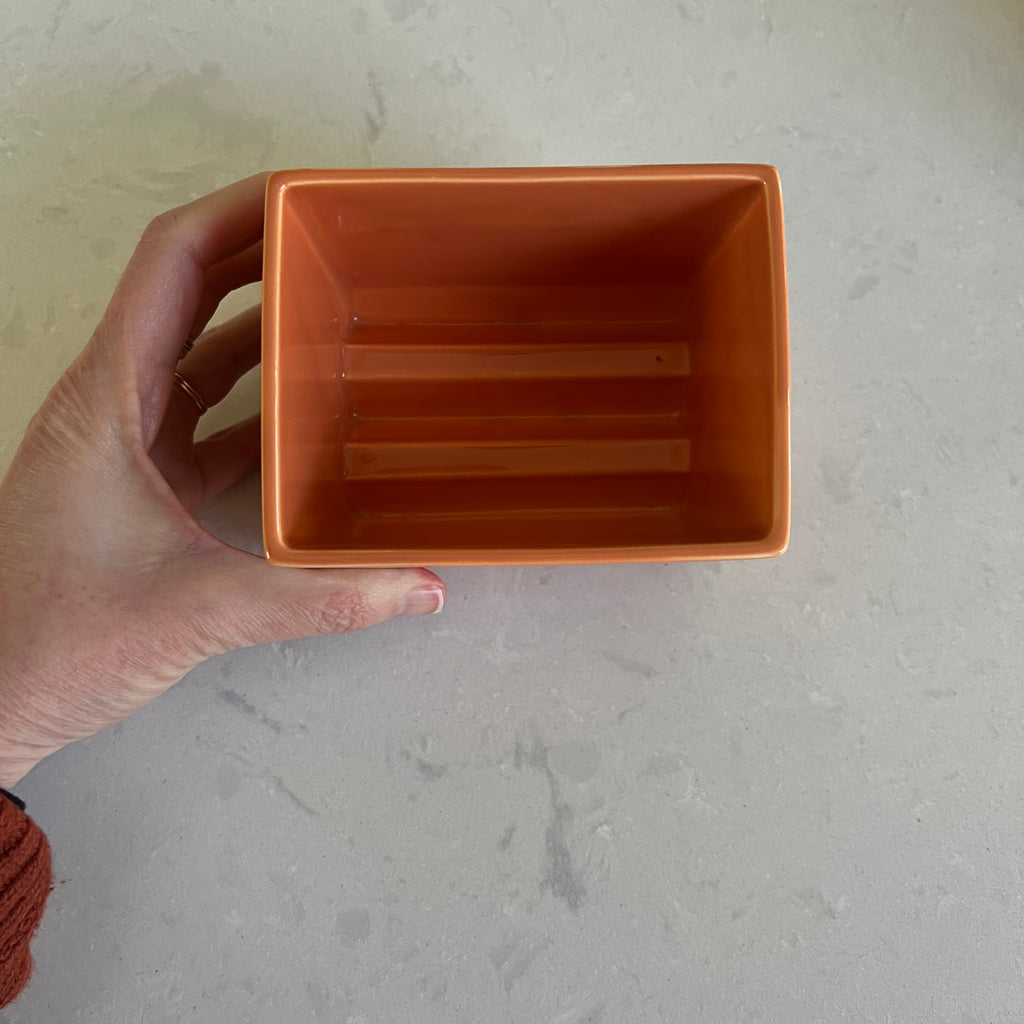 Hand holding a small ceramic box against a neutral background