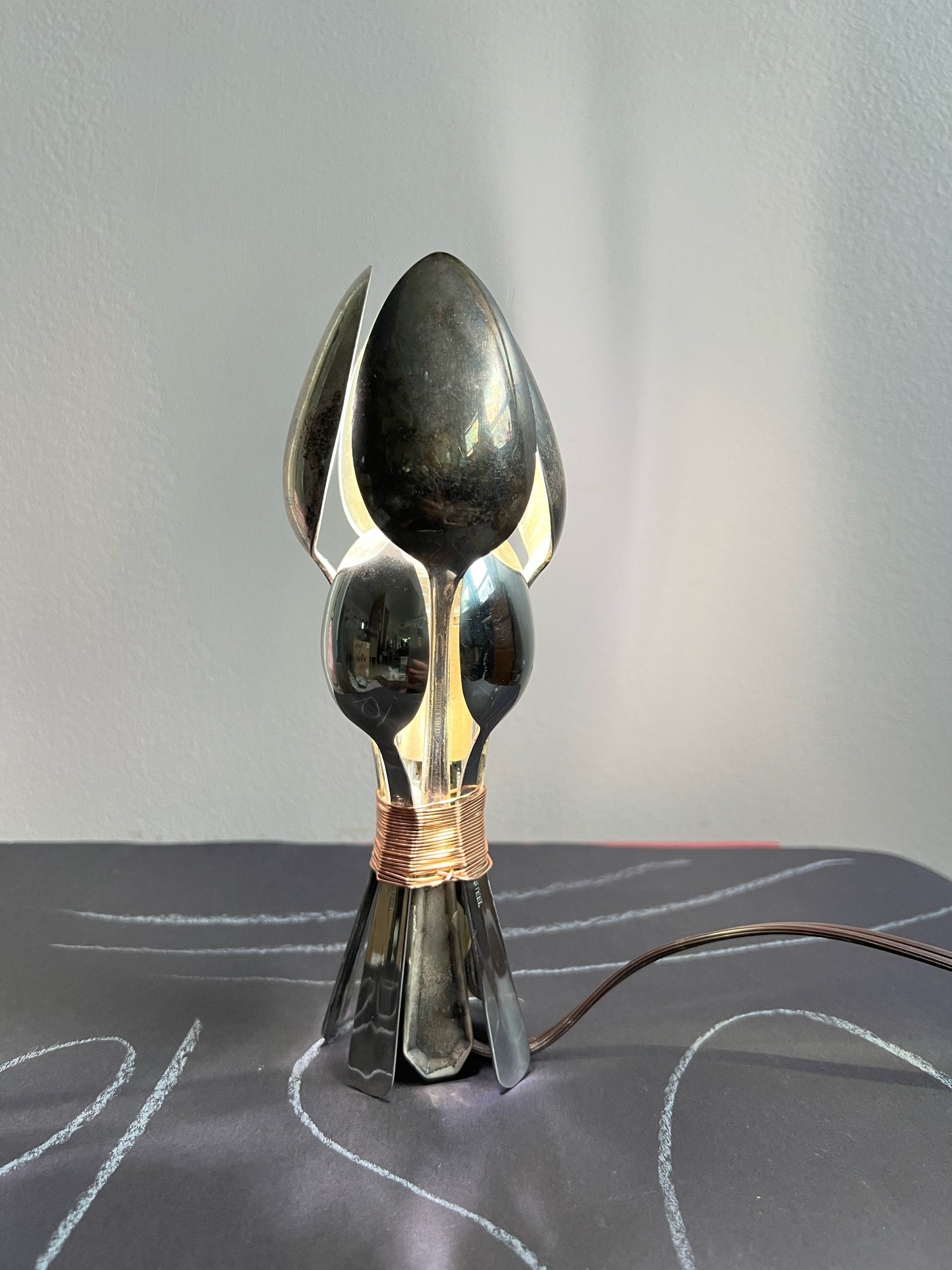 Lamp made of  metal spoons on a gray surface.