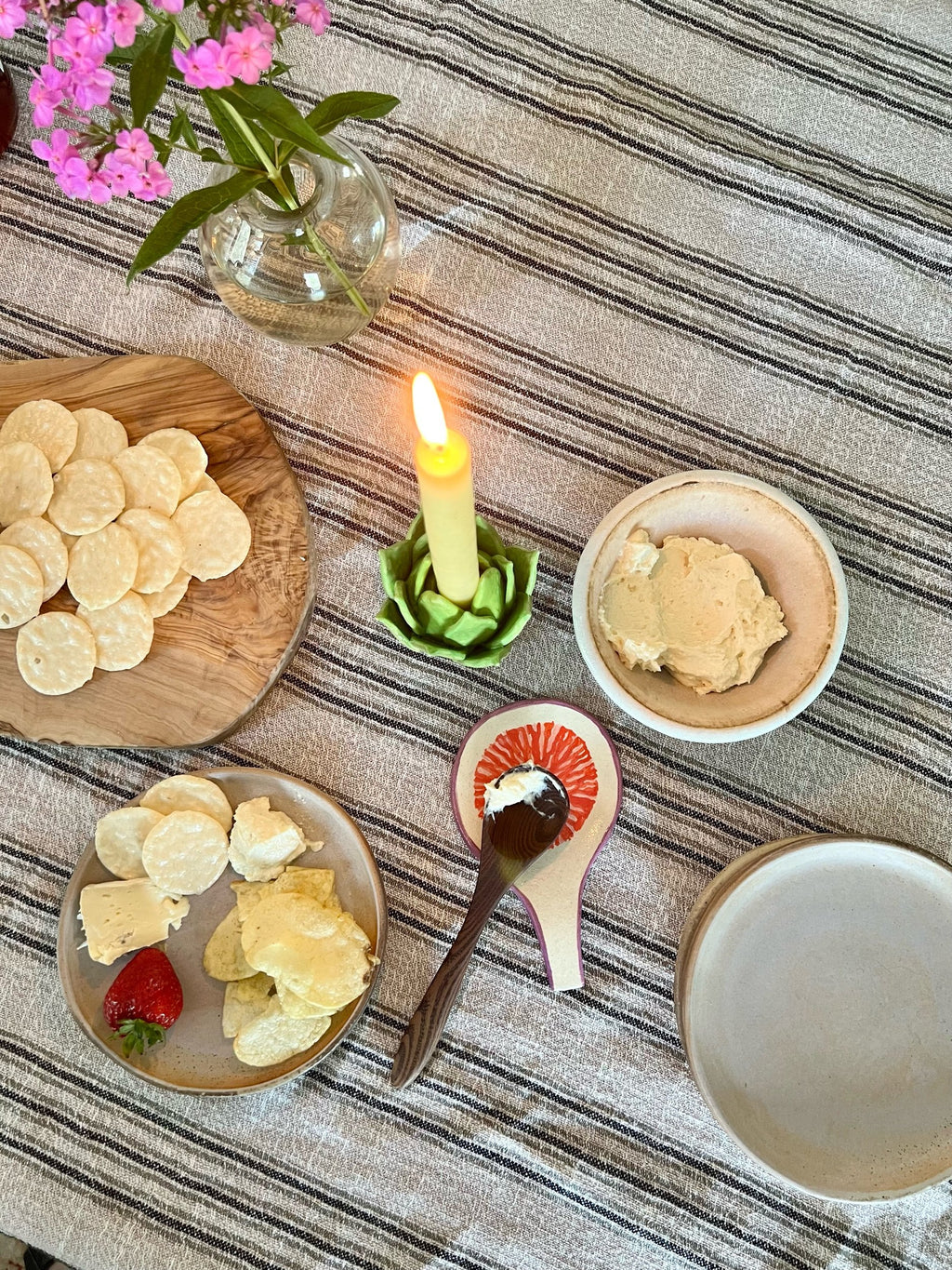 Table setting with crackers, a candle, and a bowl of spreadable food on a striped tablecloth.