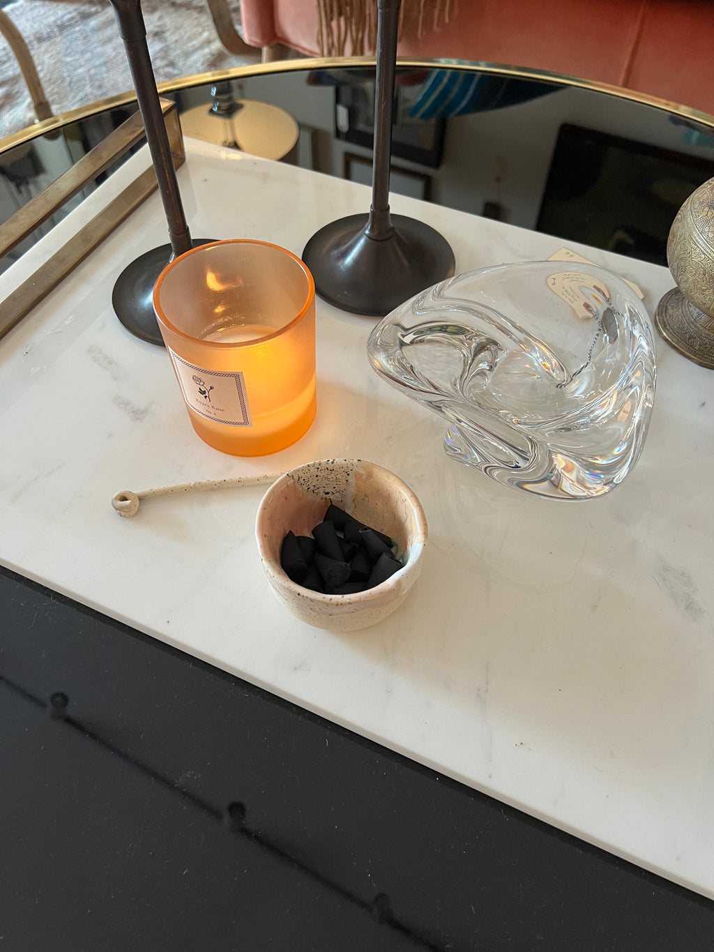 Candle, small bowl with incense cones, and glass bowl on a marble surface.