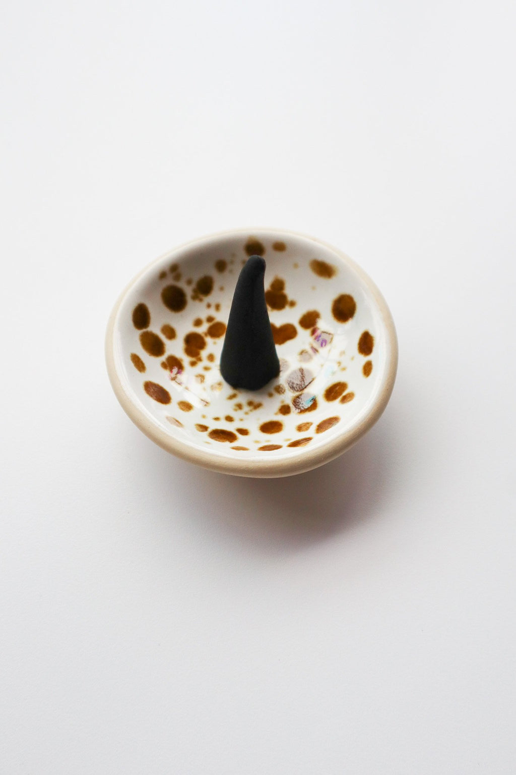 Ceramic dish with spotted design containing a black incense cone on a white background