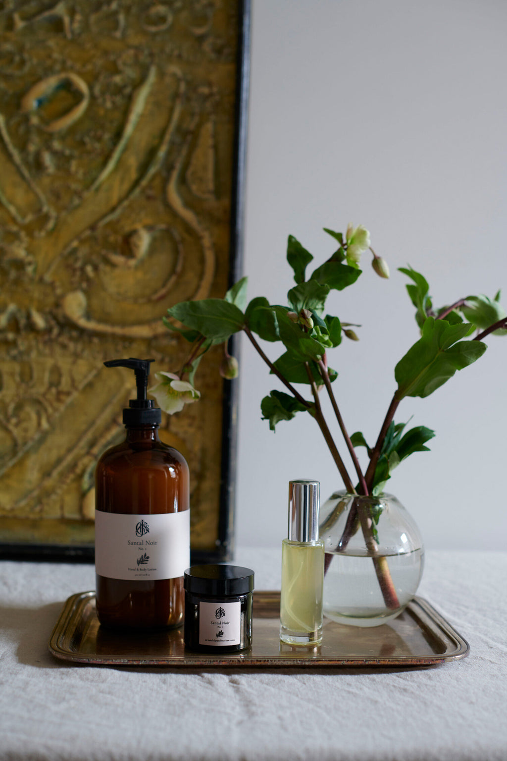 Lotion bottle and a vase with greenery on a tray against a decorative wall.