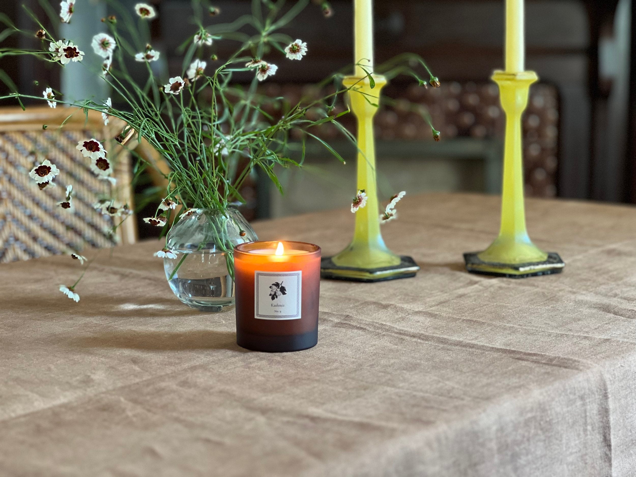 Candle with a label on a table with flowers and candles in the background
