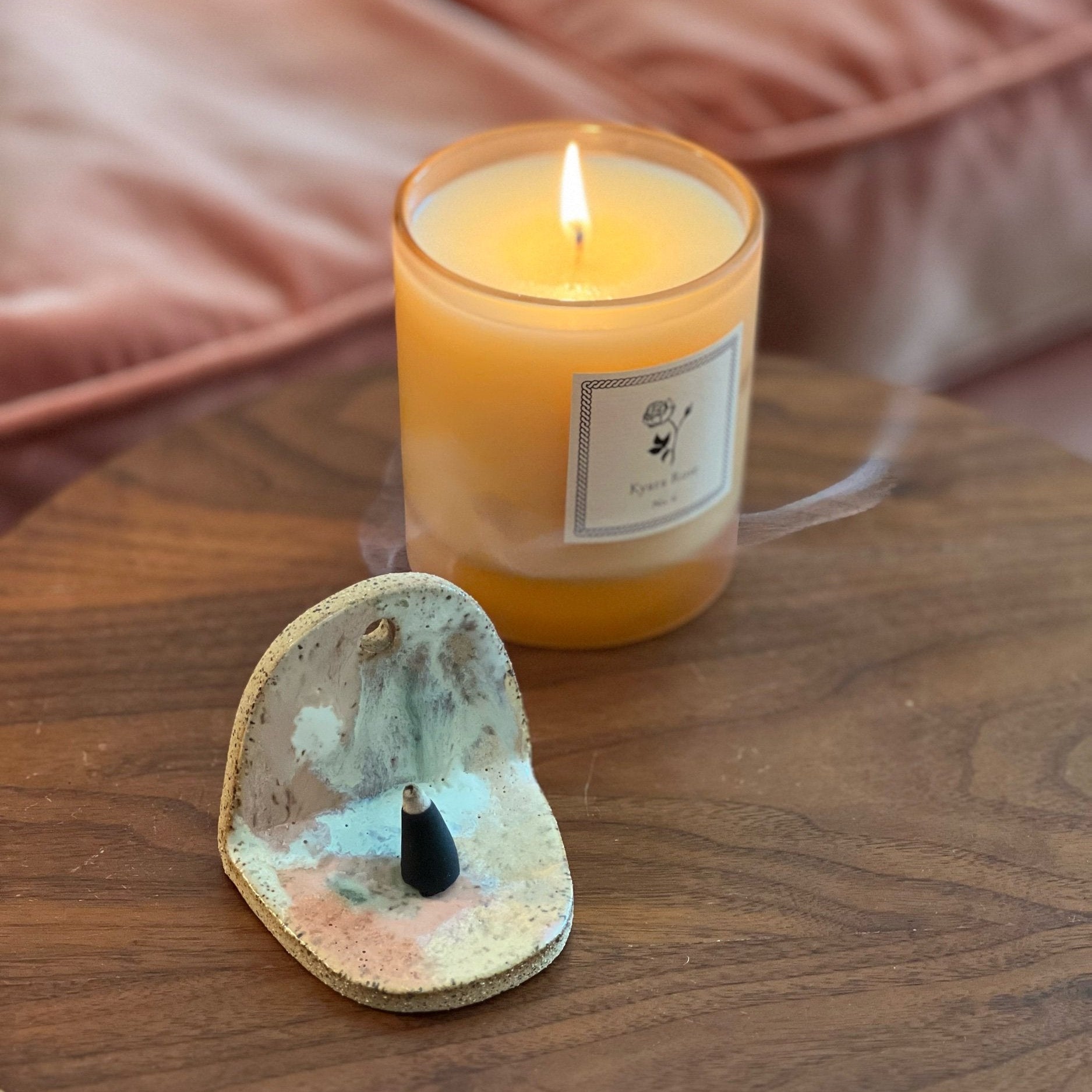 Kyara Rose Candle on a wooden table next to a ceramic incense altar. 