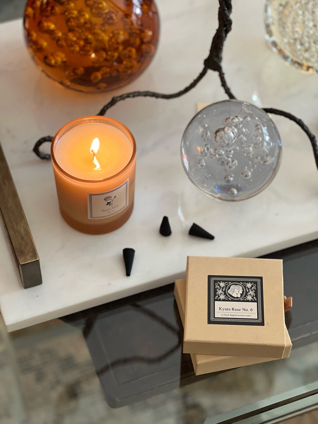 Candle burning on a marble surface with decorative items and a two boxes of Kyara Rose incense. 