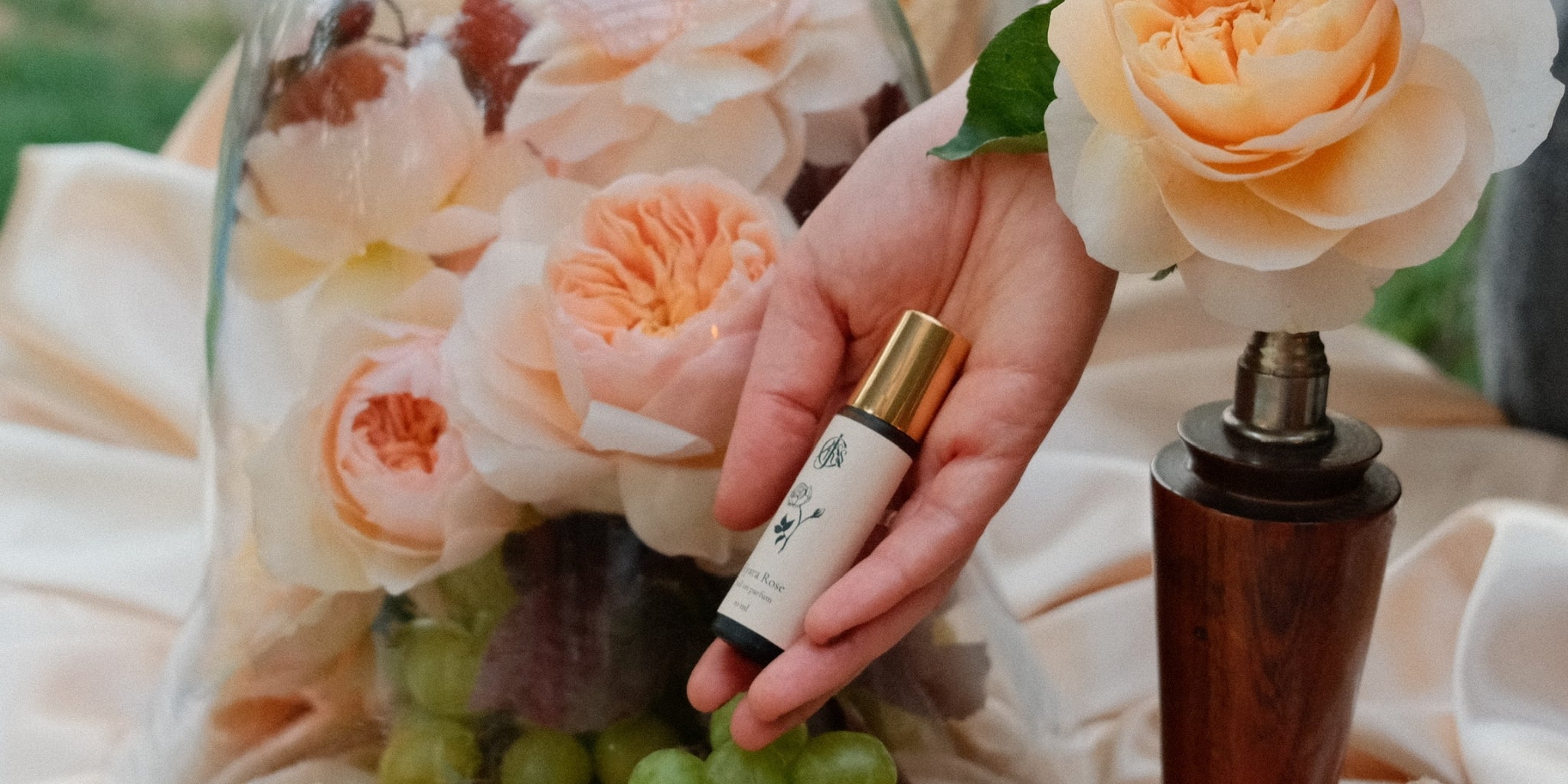 Hand holding a bottle of perfume next to a vase of flowers