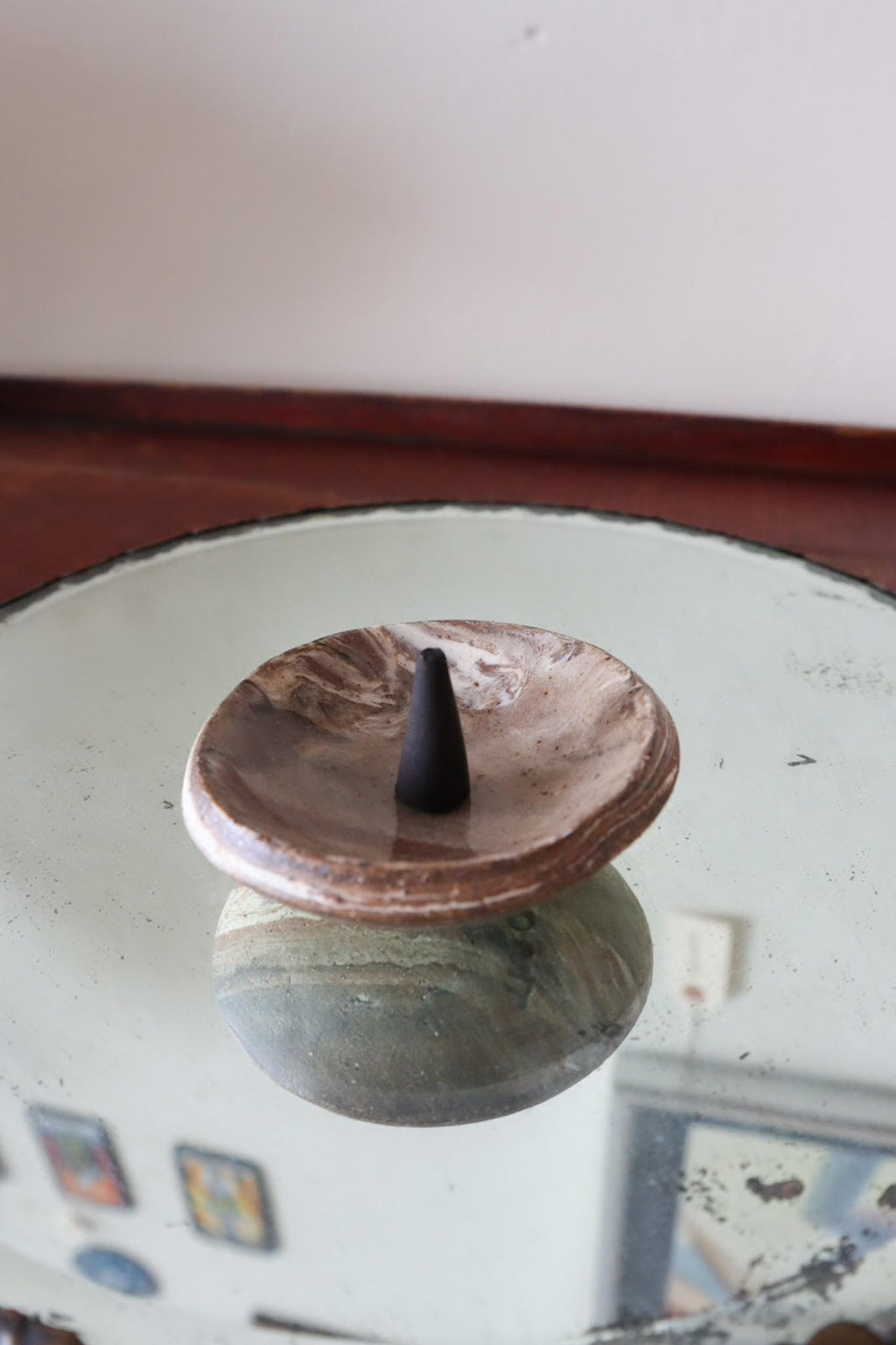 Black incense cone on a ceramic dish over a reflective surface with a blurred background