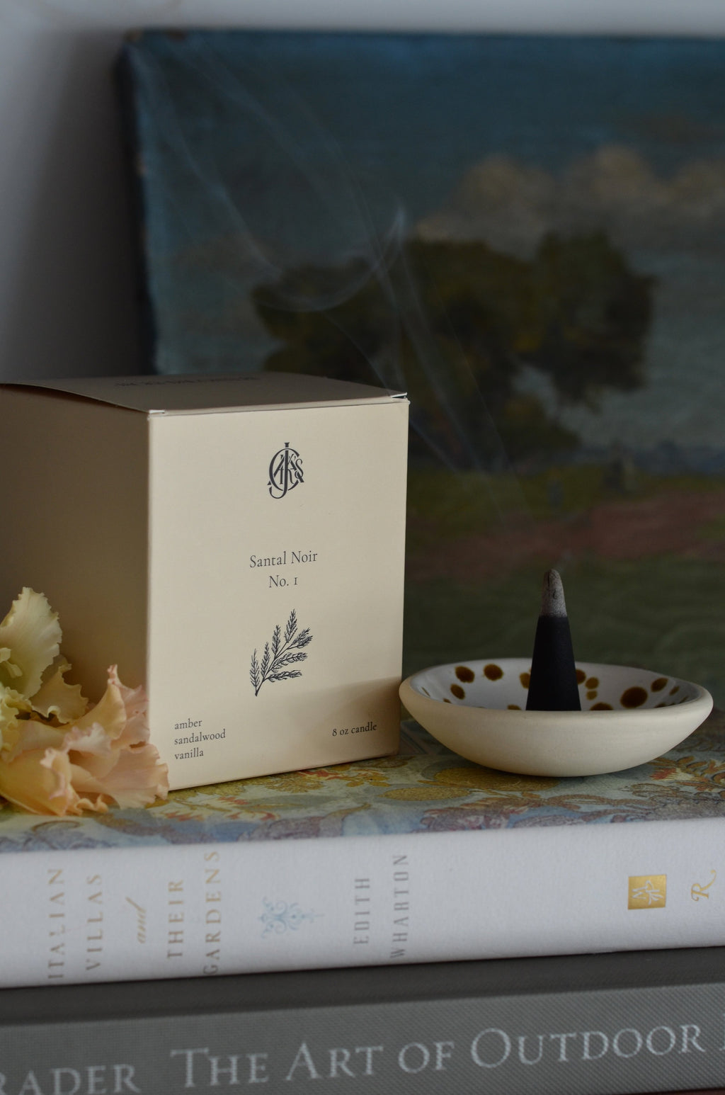 Incense cone holder with a cone on top of a book next to a box labeled 'Sandal Noir No. 1' against a blurred background.