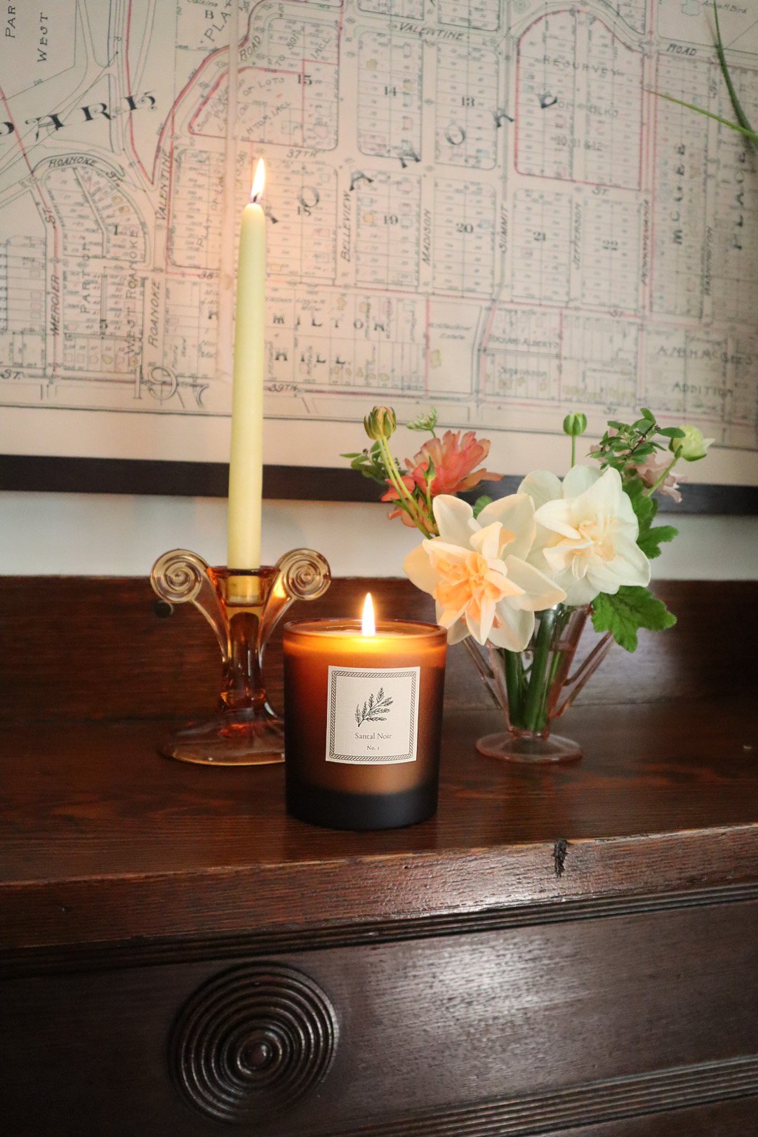 Candle and floral arrangement on a wooden mantel with a map in the background