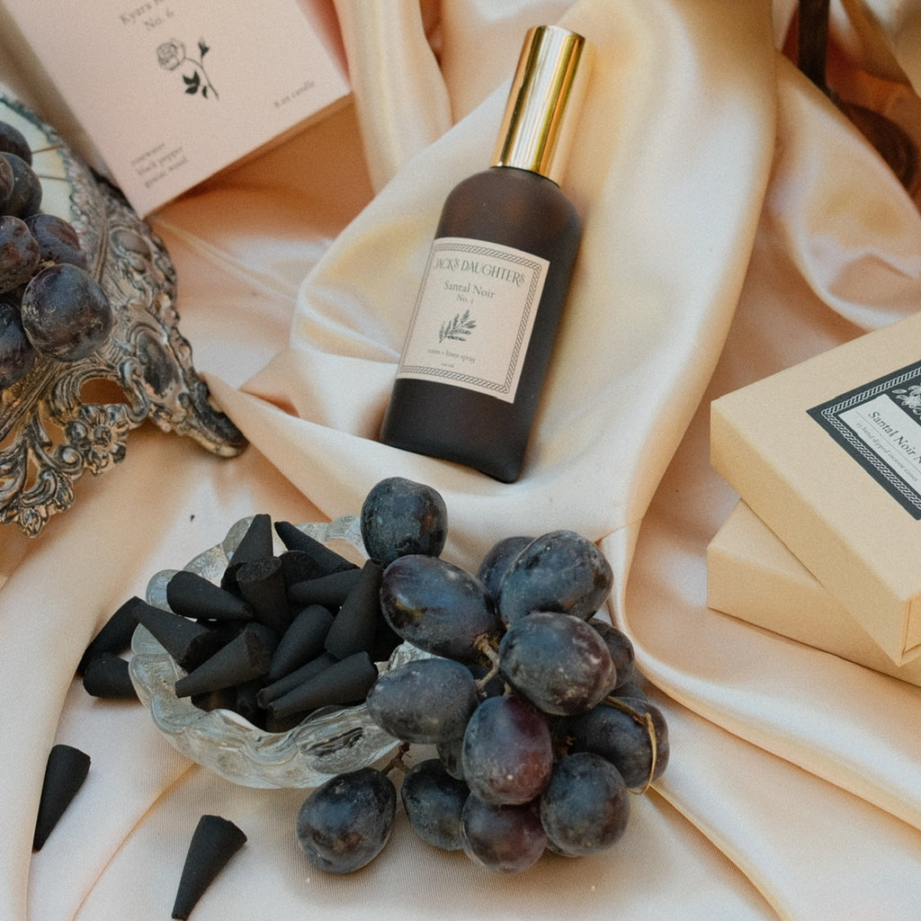 Perfume bottle, grapes, and incense cones on a soft fabric background