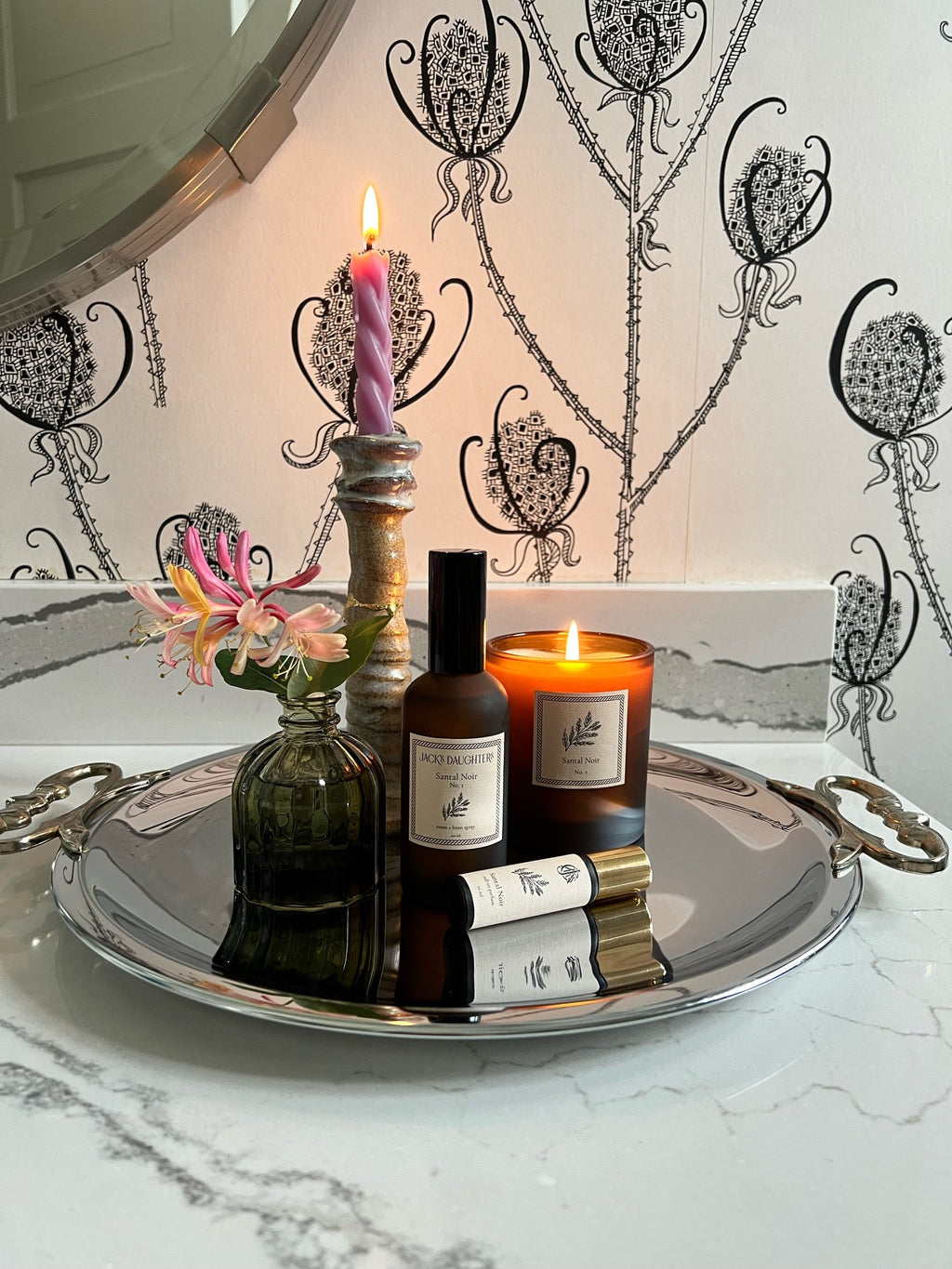 Decorative tray with candles, flowers, and bottles on a marble surface.