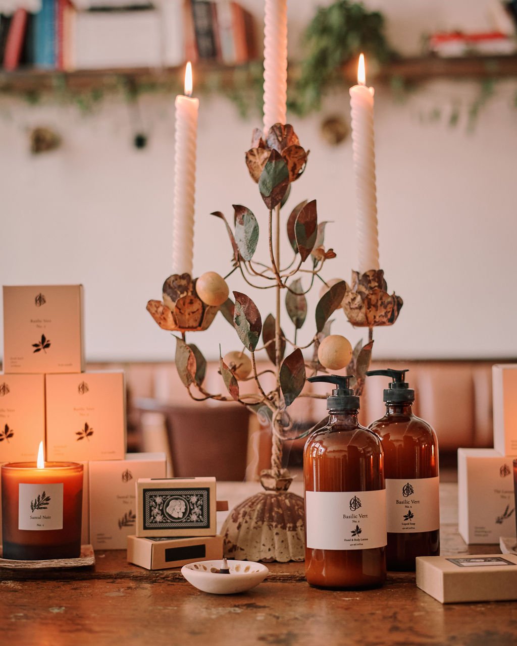 Decorative setup with candles, soap and lotion bottles, and a decorative metal piece on a wooden surface.