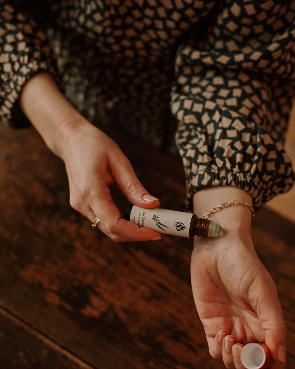 Person holding roll on parfum bottle with against a wooden surface.