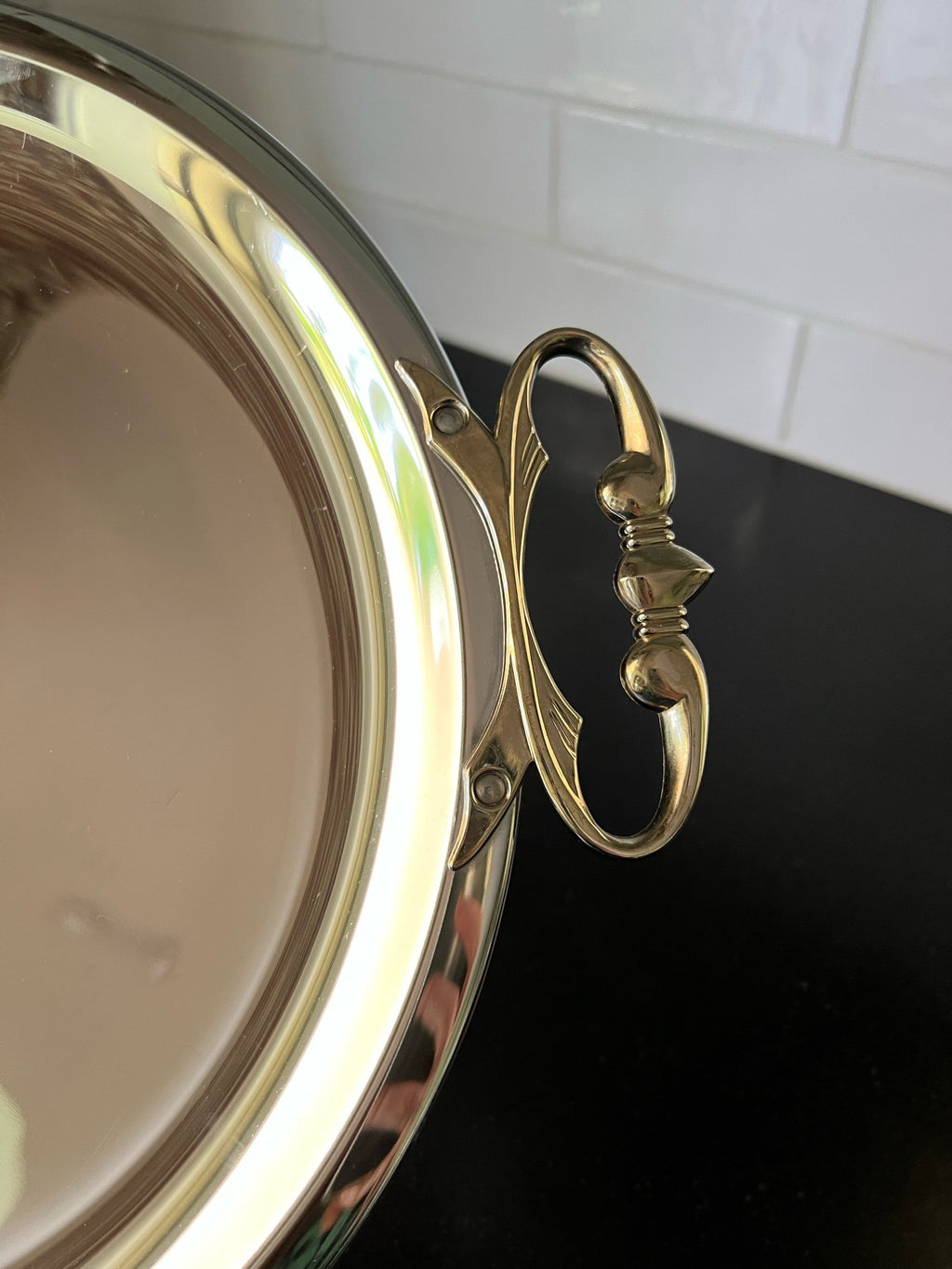 Close-up of a kromex tray with decorative handle against a white tiled wall.