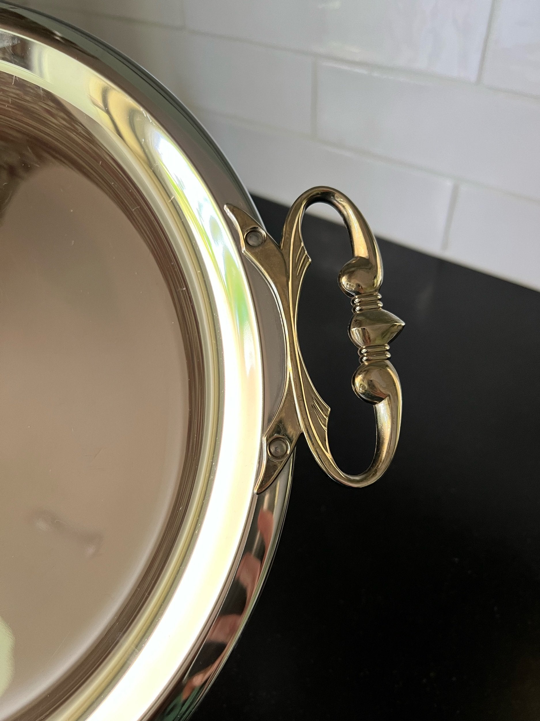 Close-up of a kromex tray with decorative handle against a white tiled wall.