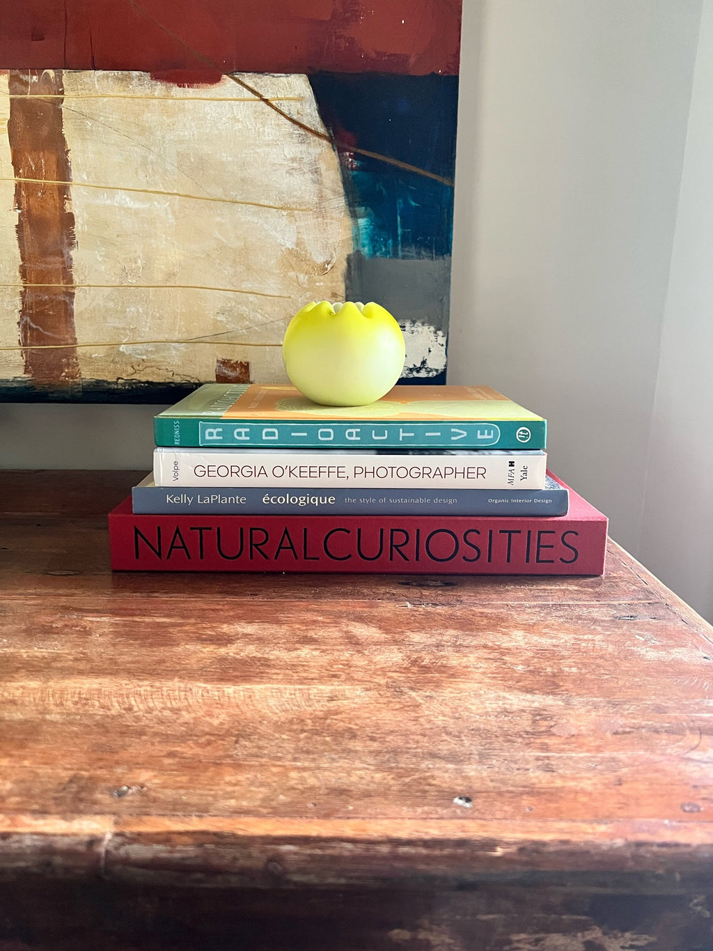 Stack of books on a wooden surface with yellow satin glass vase on top