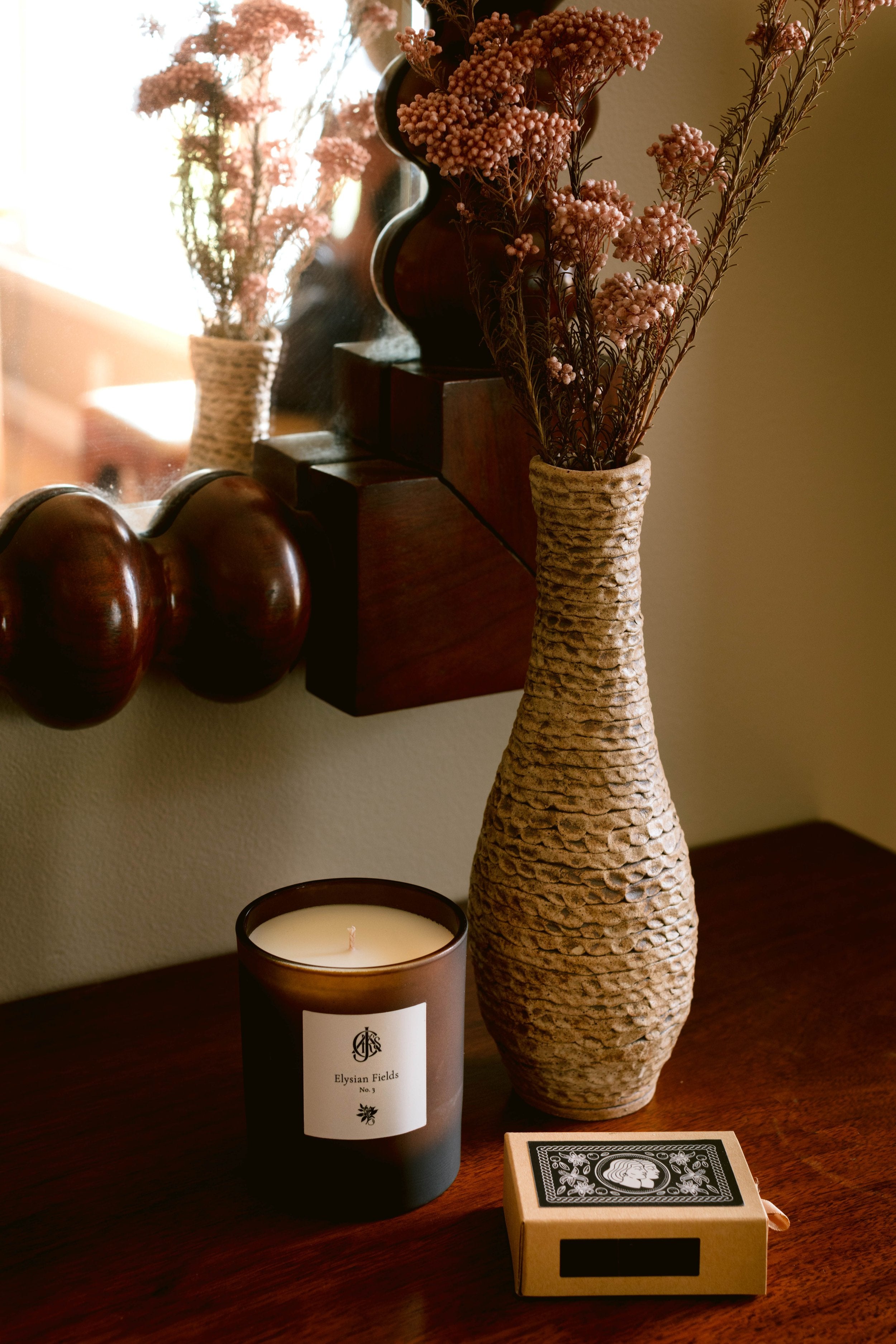 Candle with a label and decorative vase on a wooden surface