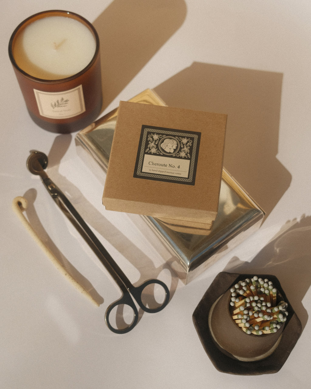 A white tabletop featuring a candle and candle accessories with sunlit shadows.