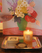 Incense cone being lit over a tray with a floral painting in the background.