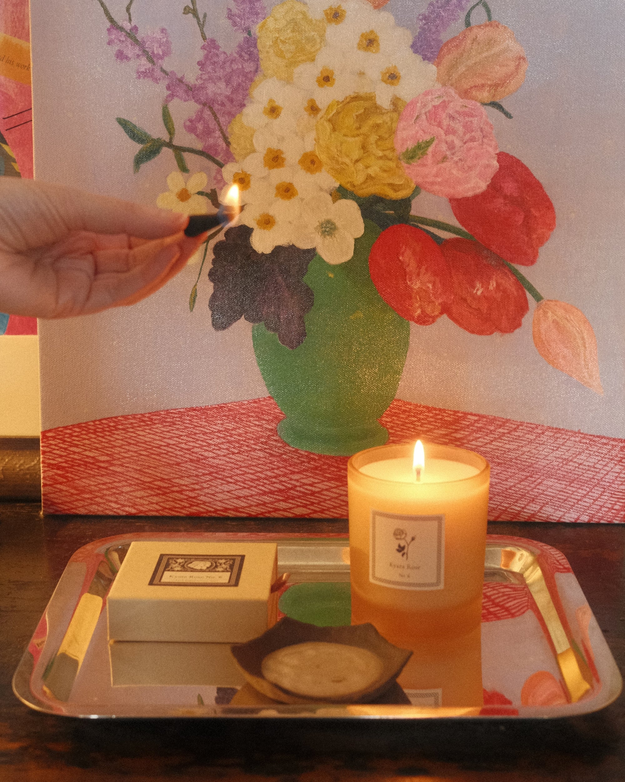 Incense cone being lit over a tray with a floral painting in the background.