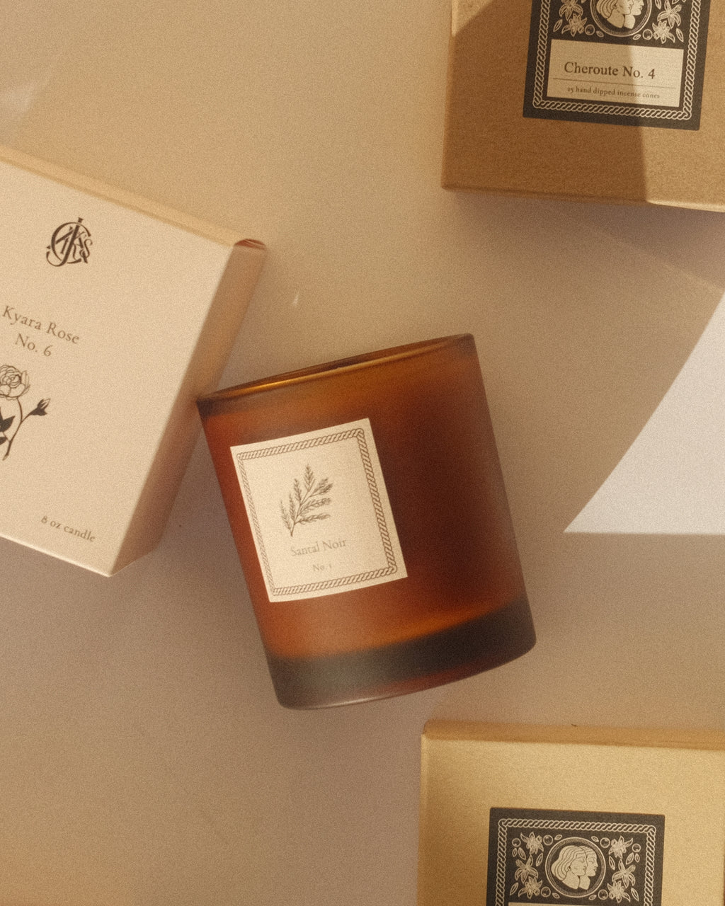 Amber glass candle and boxes with Jack's Daughters branding on a beige surface.