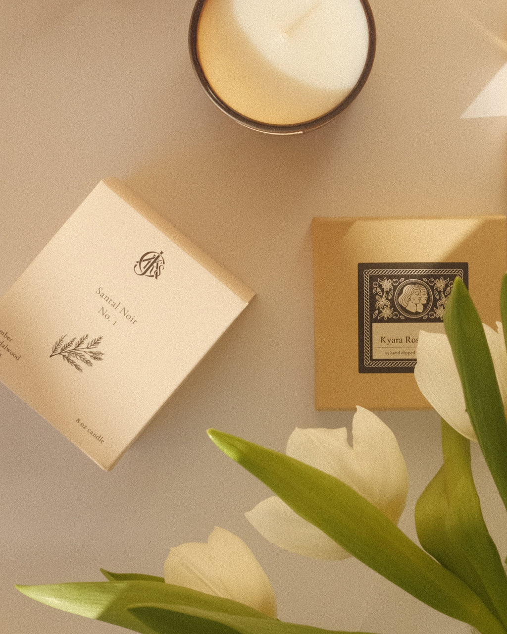 A simple sunlit arrangement of a candle, candle box, and white tulips.