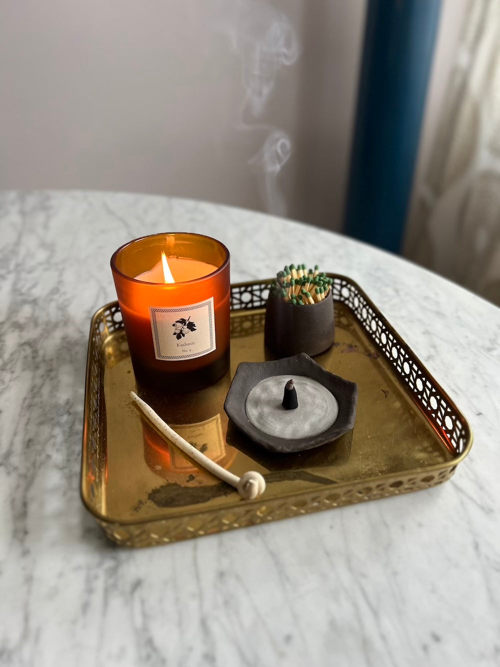 Candle on a decorative gold tray with an incense dish and match striker on a marble surface