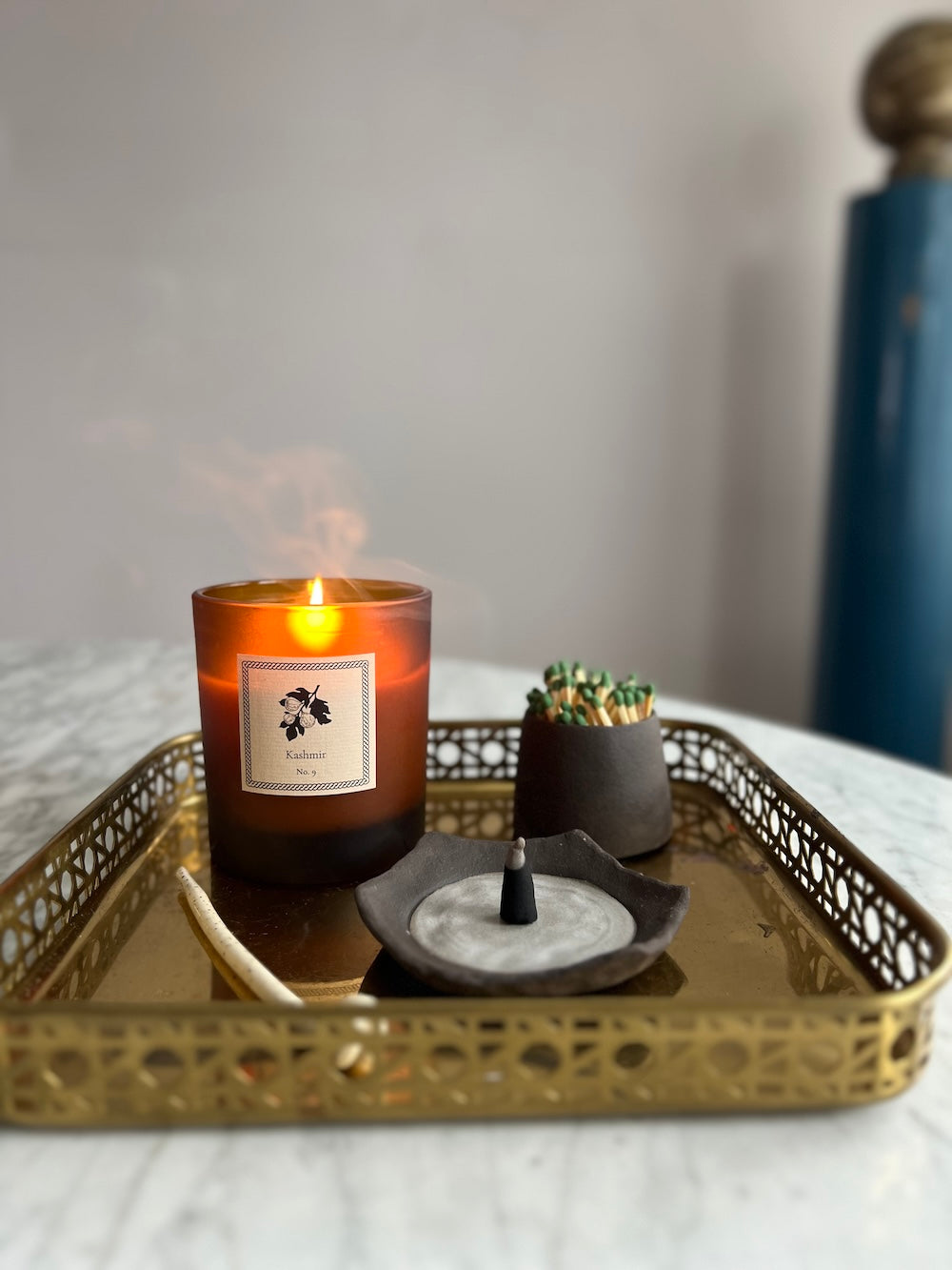 Candle with a label on a decorative gold tray with a incense dish and a match striker.