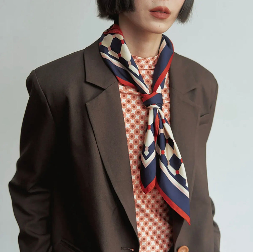 A model wearing a brown blazer and blue and white checkered scarf around their neck with a white background