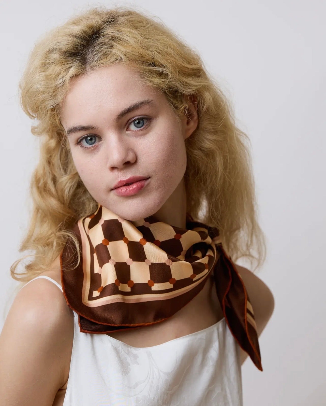 Woman wearing a brown and beige checkered scarf on a plain background